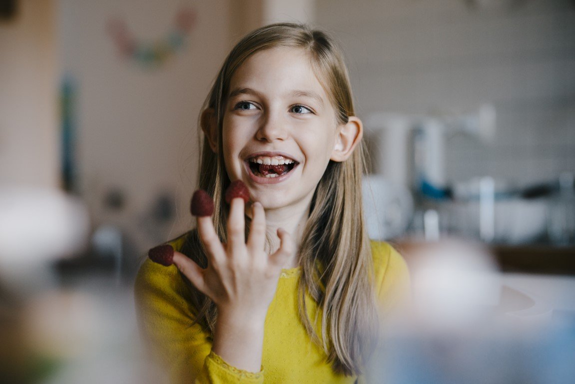 Ein Mädchen isst Himbeeren, die auf ihren Fingern stecken.